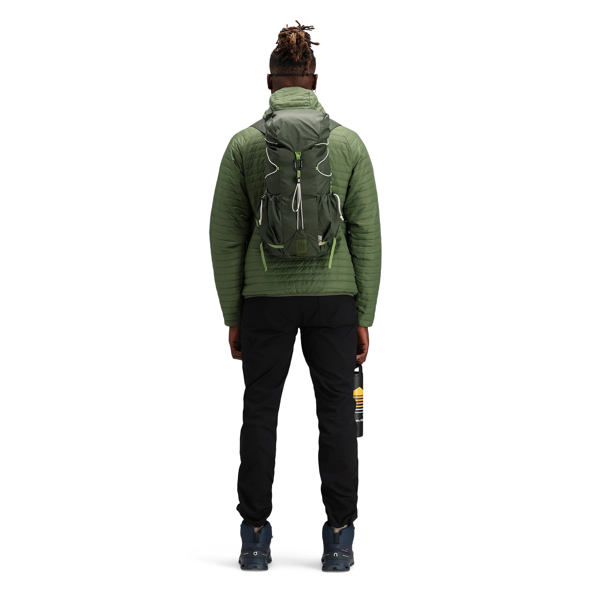 Model wearing Topo Designs TopoLite Cinch Pack 16L packable daypack backpack for travel in "olive" green.