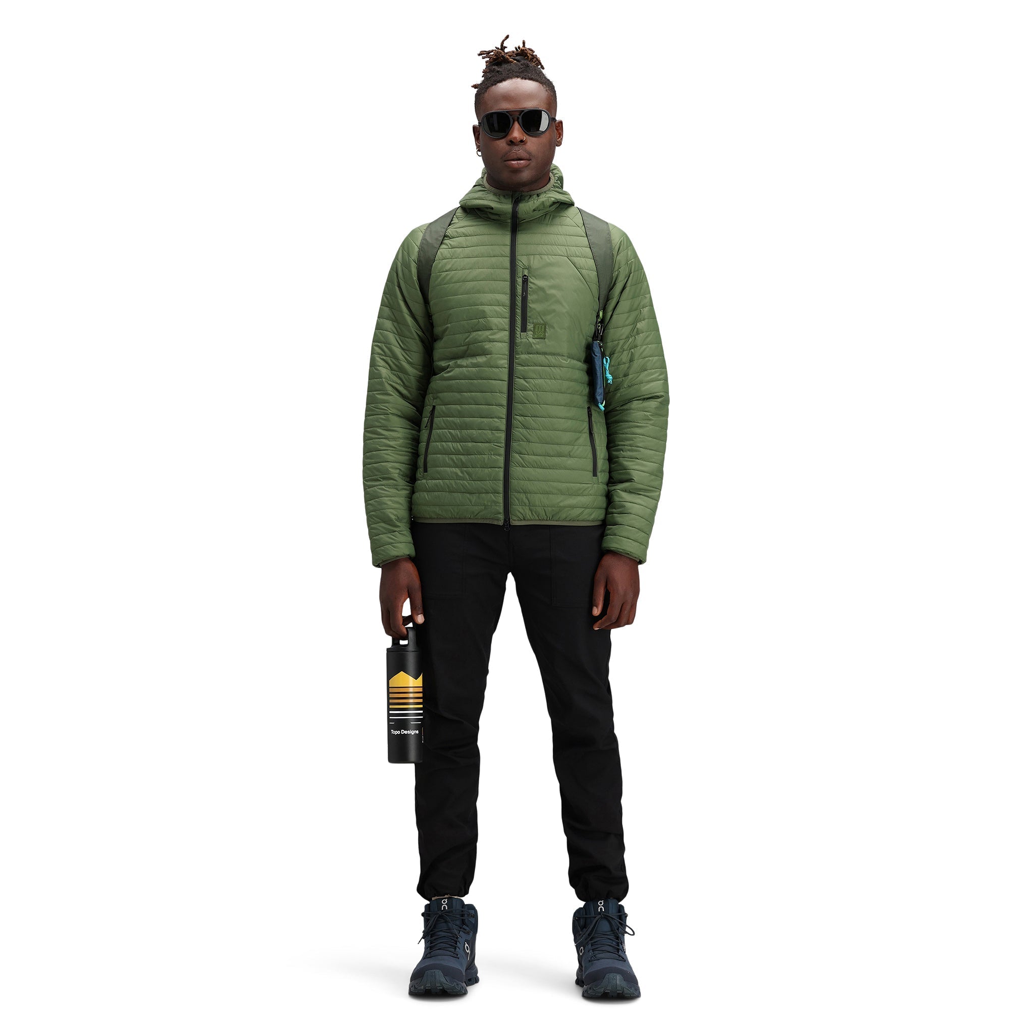 Model wearing Topo Designs Men's Global Puffer packable recycled insulated Hoodie jacket in "olive" green.