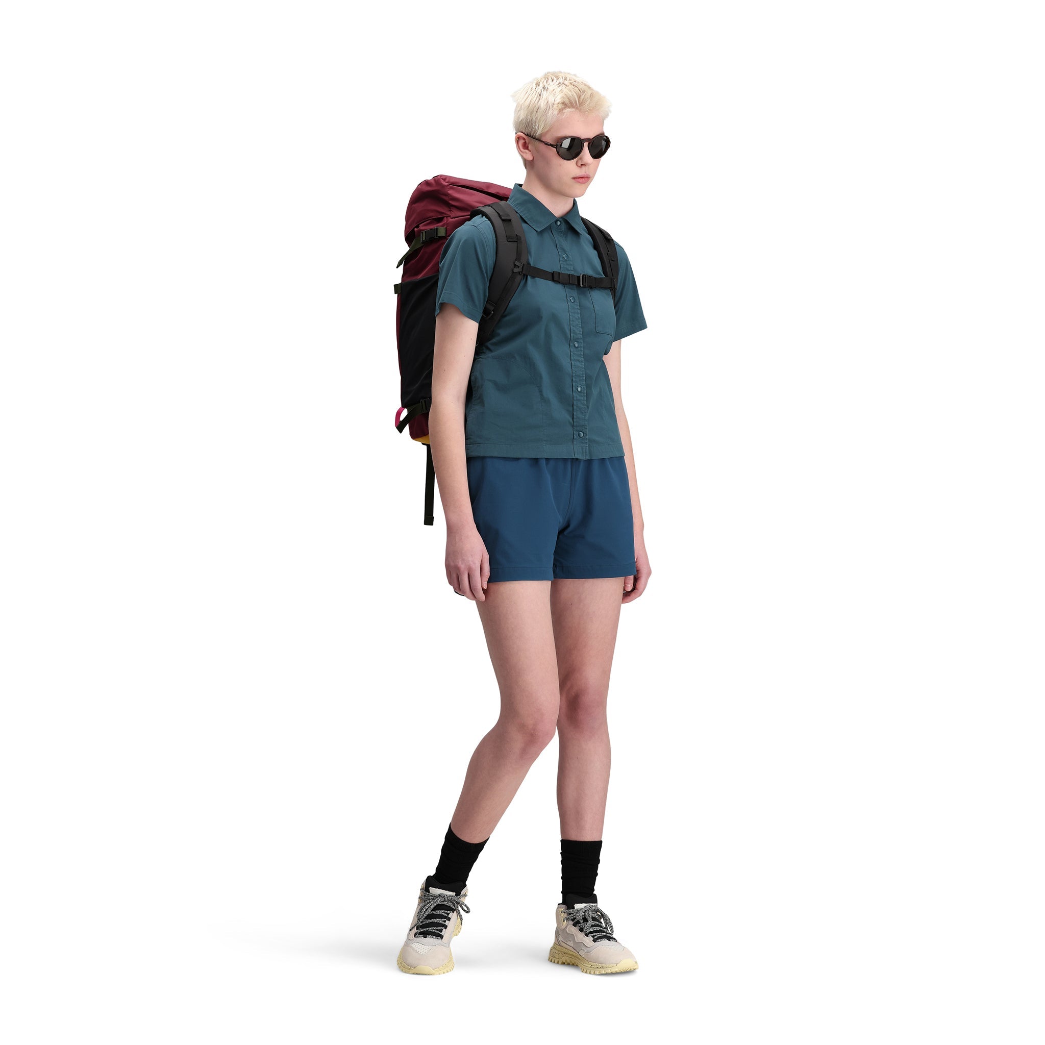  Front model shot of Topo Designs Women's Global Shirt Short Sleeve 30+ UPF rated travel shirt in "Pond Blue" green. Show on "brick".