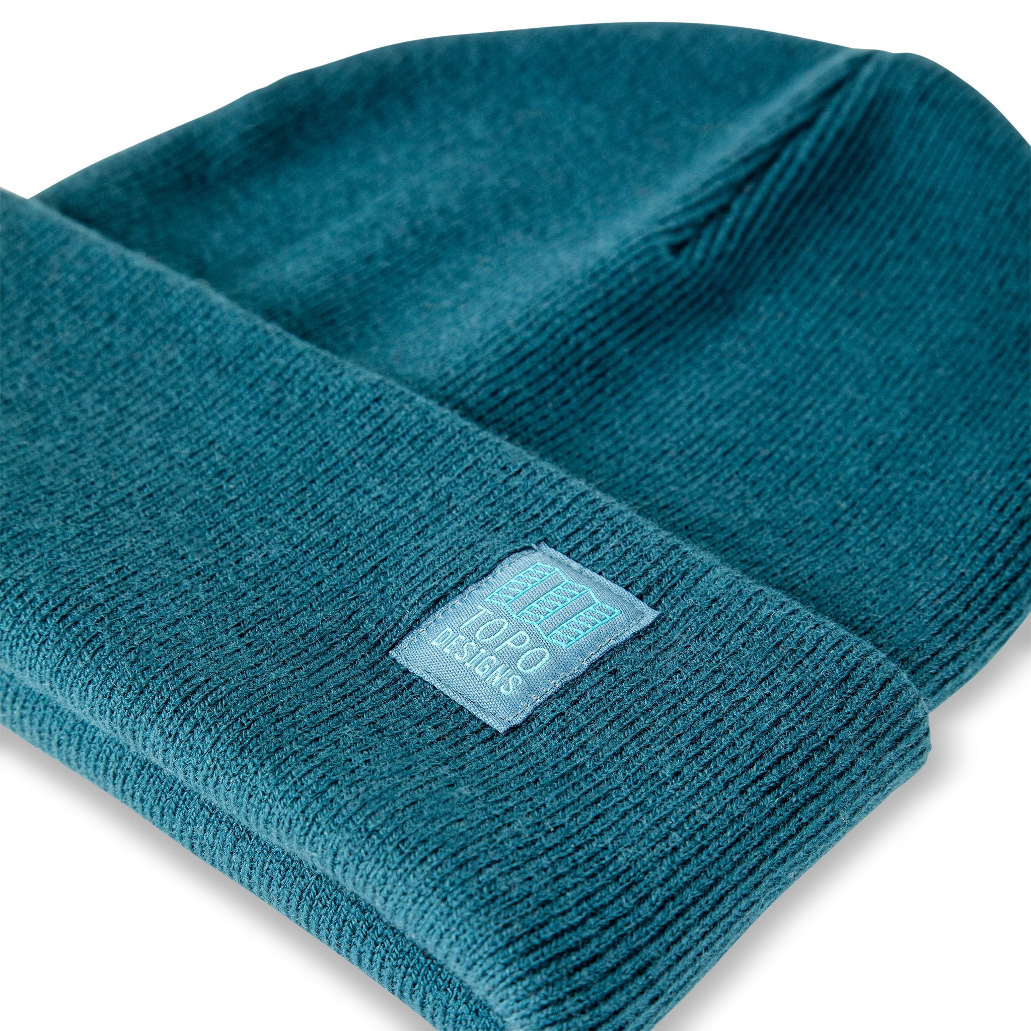 Detail shot of logo patch on Topo Designs Work Cap cuffed beanie in pond blue.