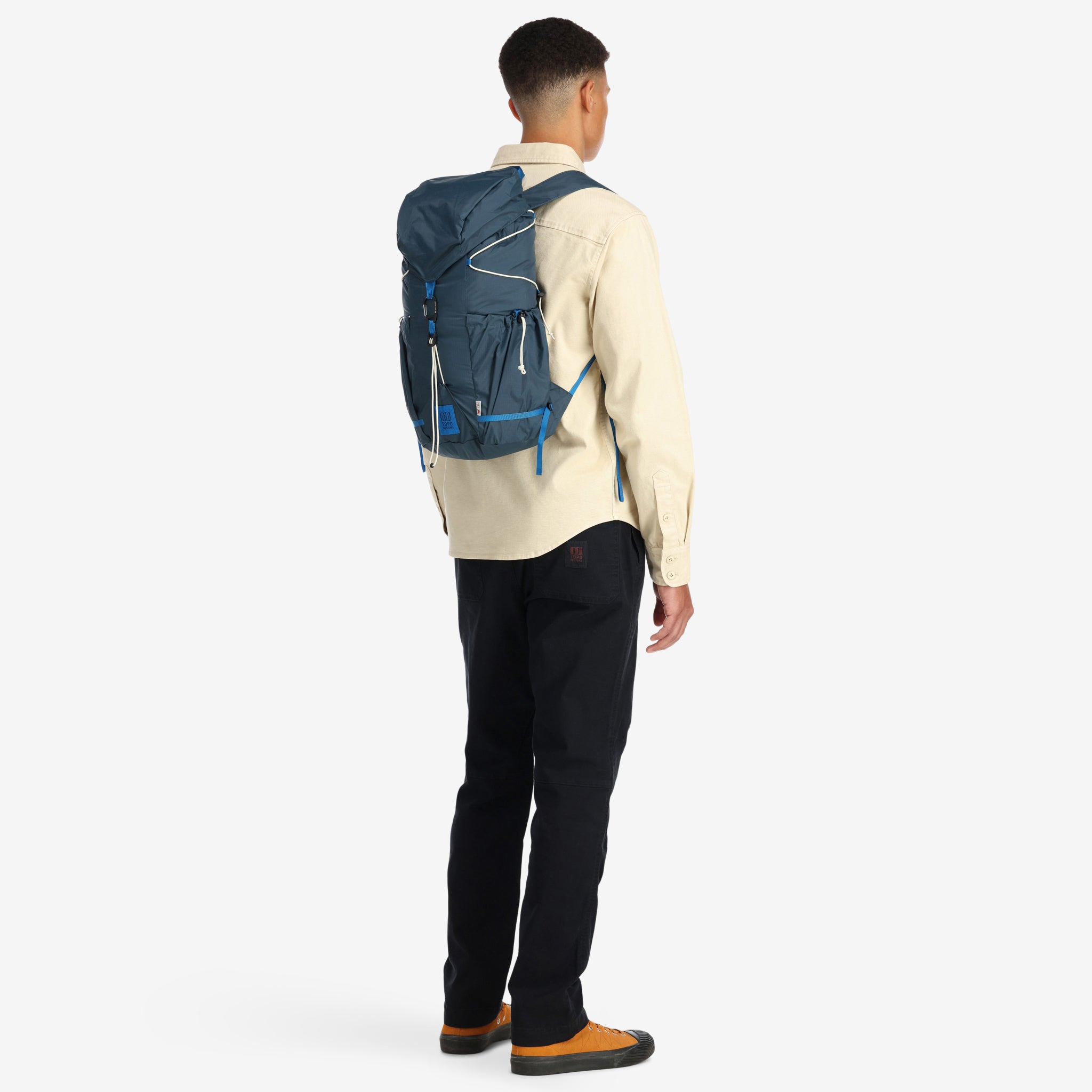 Model wearing Topo Designs TopoLite Cinch Pack 16L packable daypack backpack for travel in "pond blue"